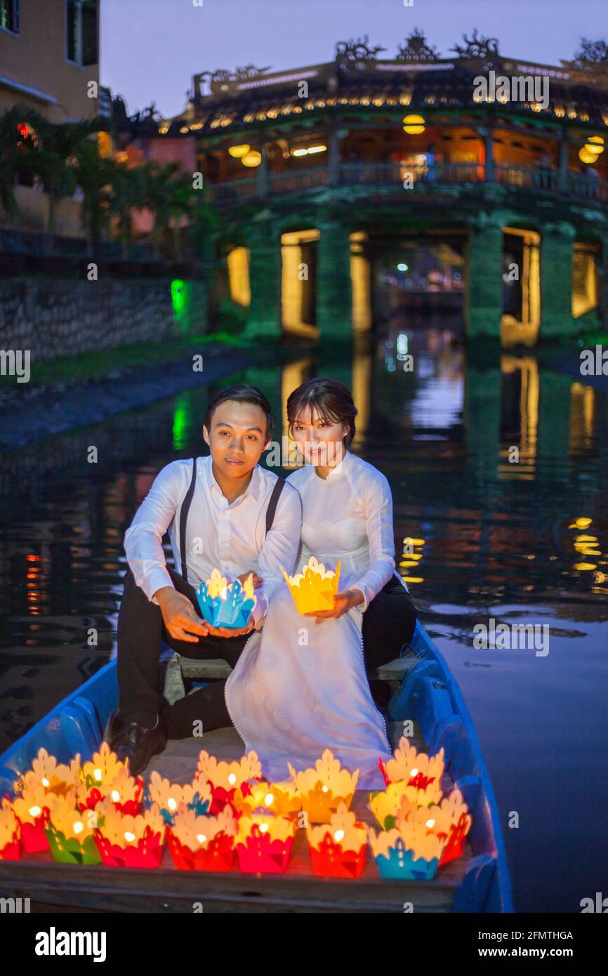 La coppia vietnamita sedette in barca di fronte al ponte giapponese rilasciare lanterne galleggianti colorati nel fiume, Hoi An, Vietnam Foto Stock