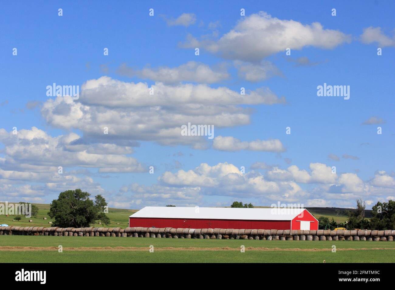 Fienile rosso del paese del Kansas con balle di fieno e cielo blu e nuvole bianche. Foto Stock