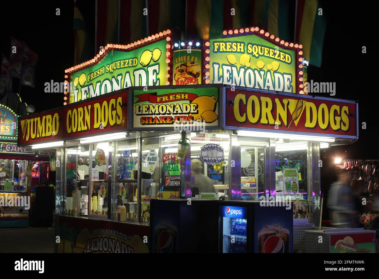 Venditore della fiera dello stato del Kansas con luci colorate di notte che vende cani da mais e limonata che è luminosa e colorata. Questo è in Kansas USA. Foto Stock