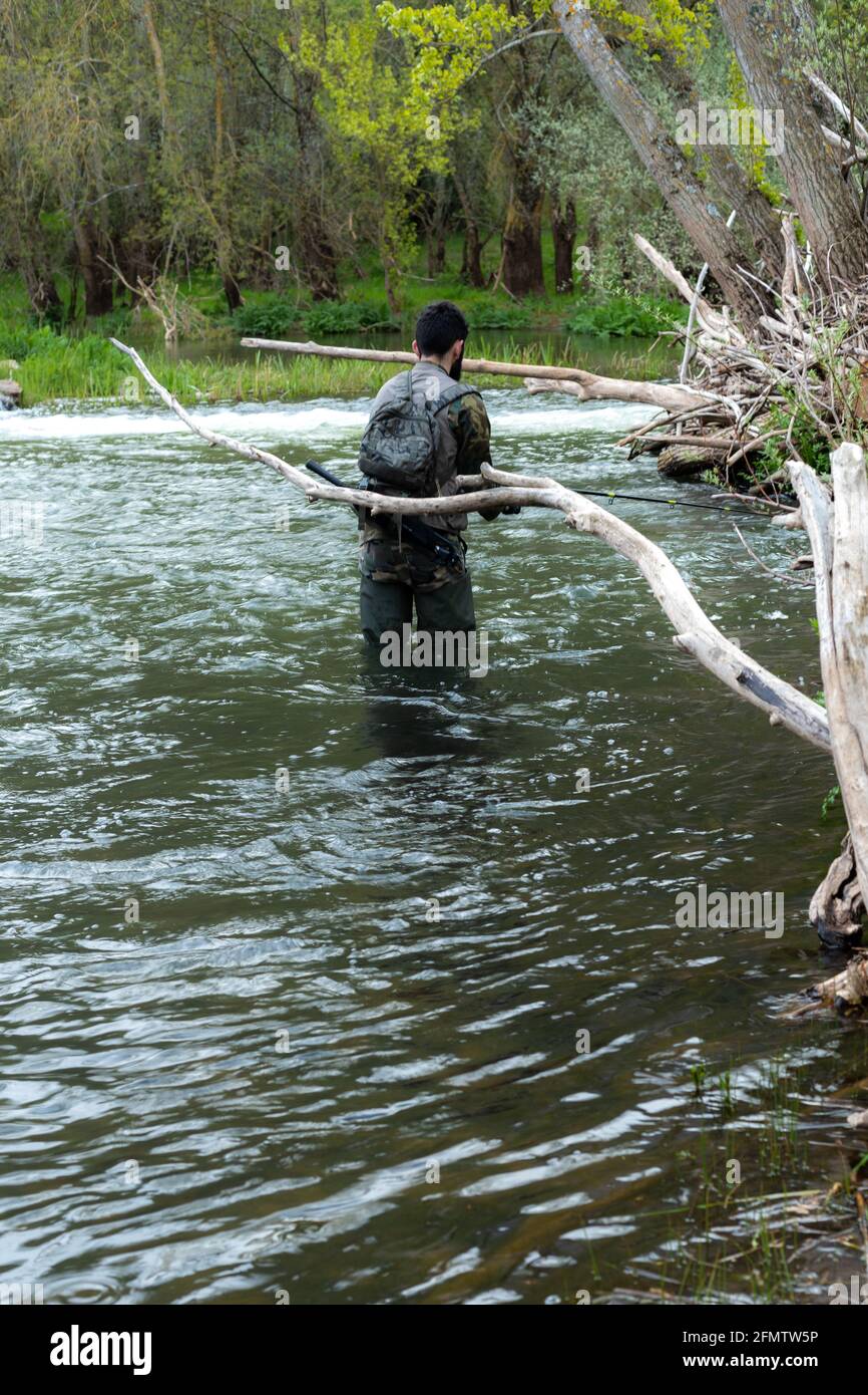 Giovane uomo sulla schiena in un fiume o ruscello con stivali da pesca in  gomma e camouflage tuta, zaino e attrezzi per lo sport della pesca con un  selettivo Foto stock 