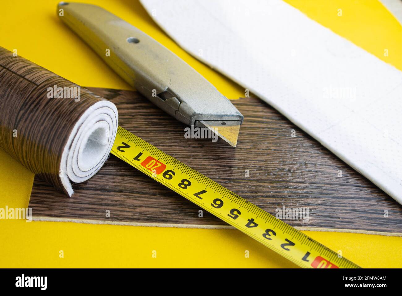 Metro a nastro in linoleum e coltello su fondo isolato. Un pezzo di linoleum. Misurazione e taglio del linoleum. Linoleum per pavimenti in PVC. Galleggiamento domestico Foto Stock