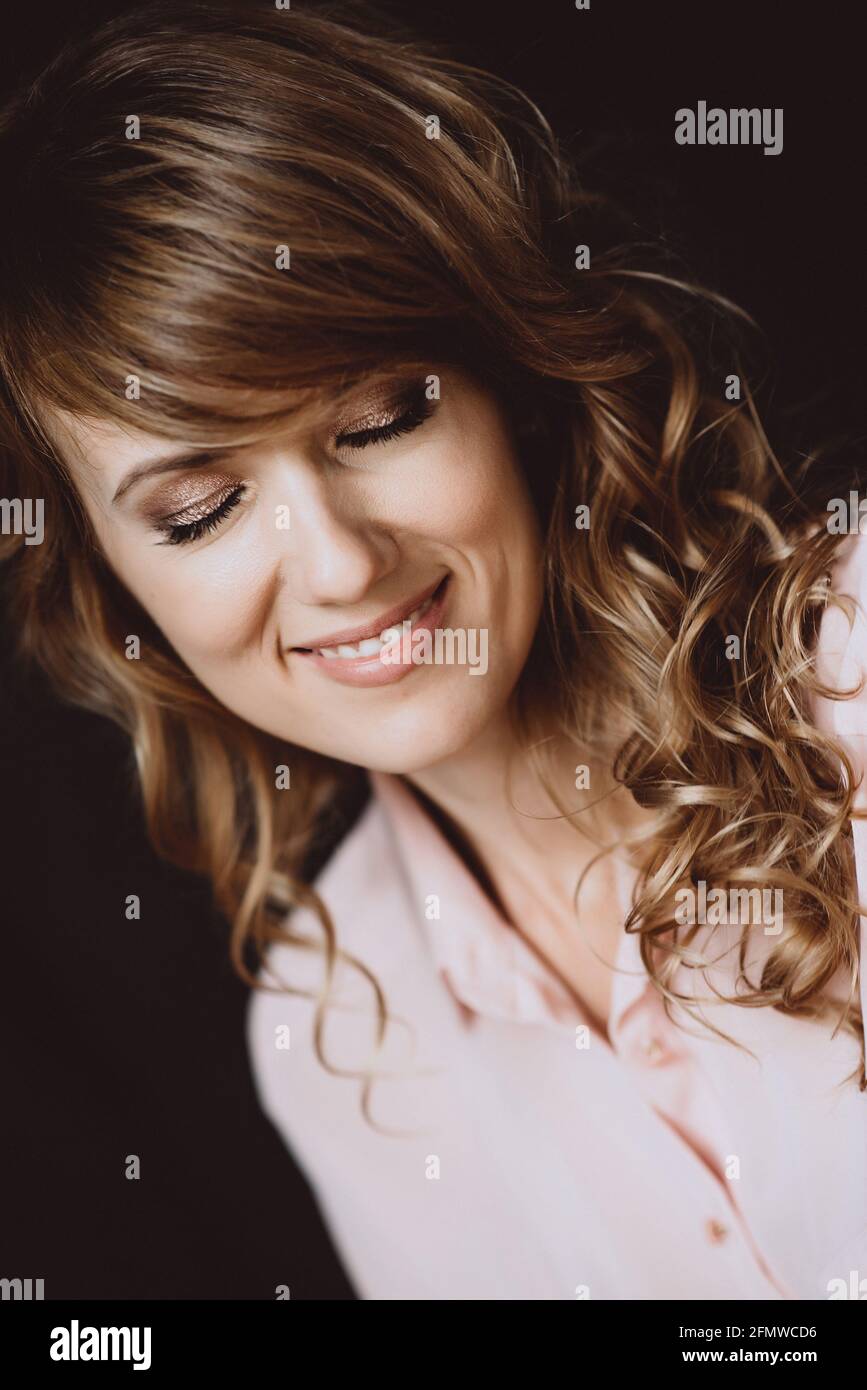 Ritratto di una bella ragazza di 36 anni con capelli ricci e un sorriso giocoso aperto e denti e occhi bianchi chiusi. Messa a fuoco selettiva morbida. Foto Stock