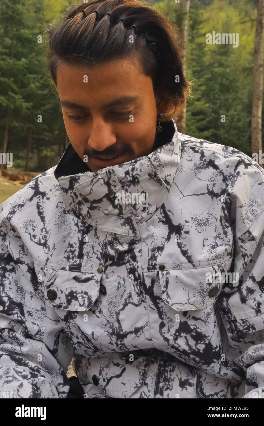 Primo piano di un giovane del Sud Asiatico che guarda giù sorridente indossando una giacca stampata bianca e nera. Foto Stock