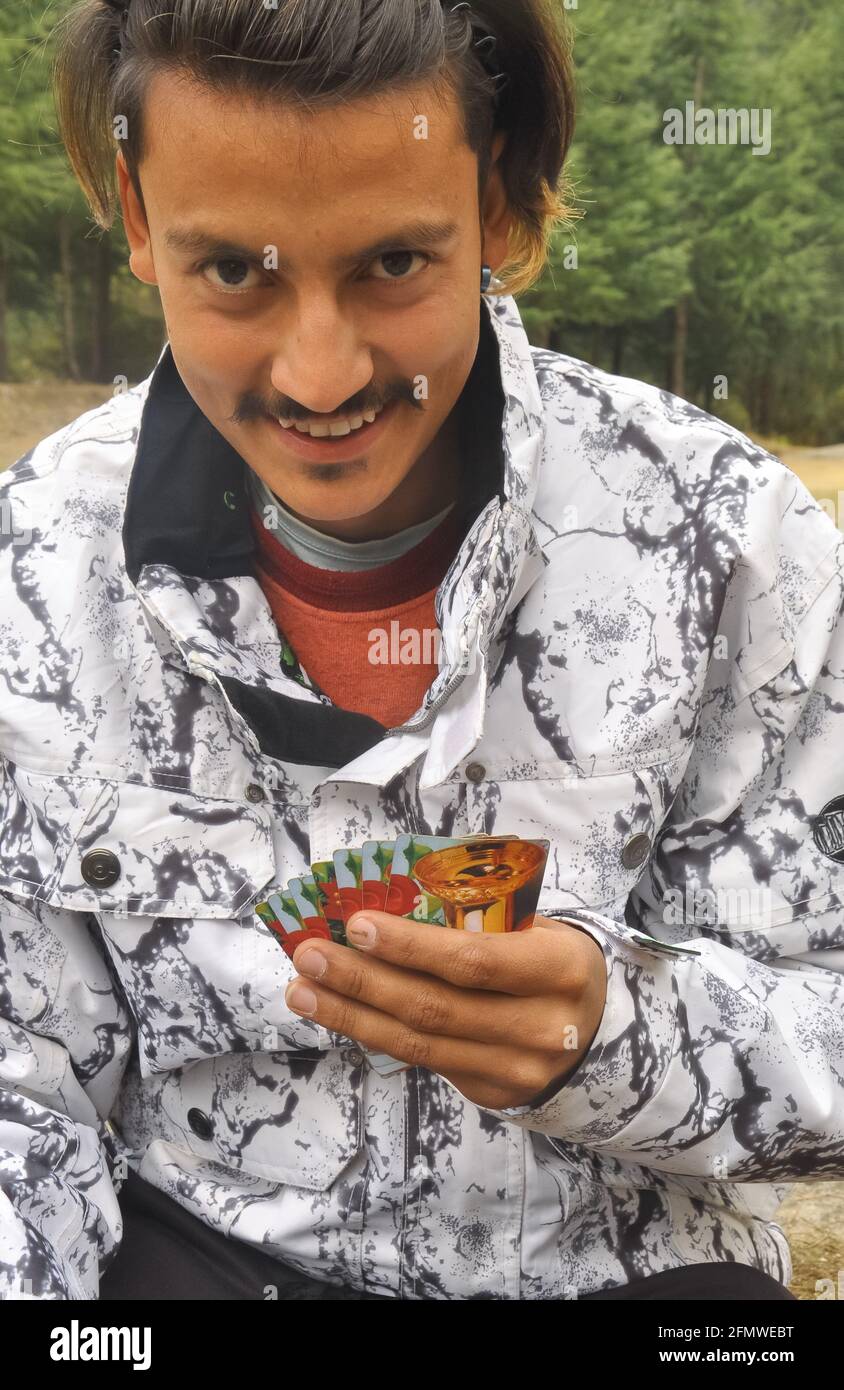 Un giovane ragazzo indiano che gioca le carte all'aperto nella stagione invernale, foto di un giovane uomo che cerca la macchina fotografica mentre gioca le carte. Foto Stock