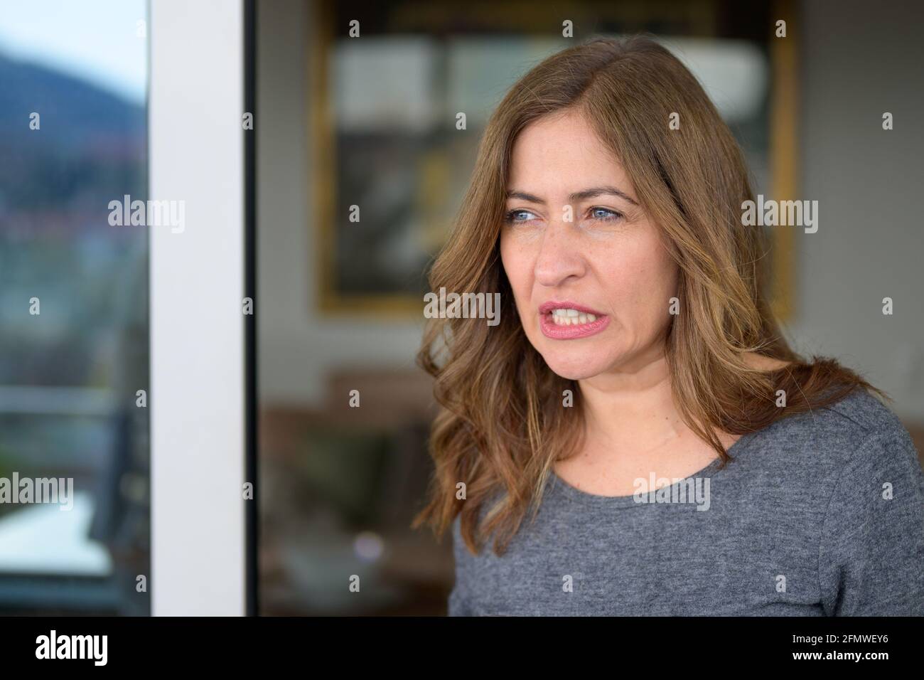 Donna premurosa che macina i suoi denti in concentrazione mentre si alza sul balcone che si affaccia sulla città sottostante con un'espressione penosa Foto Stock