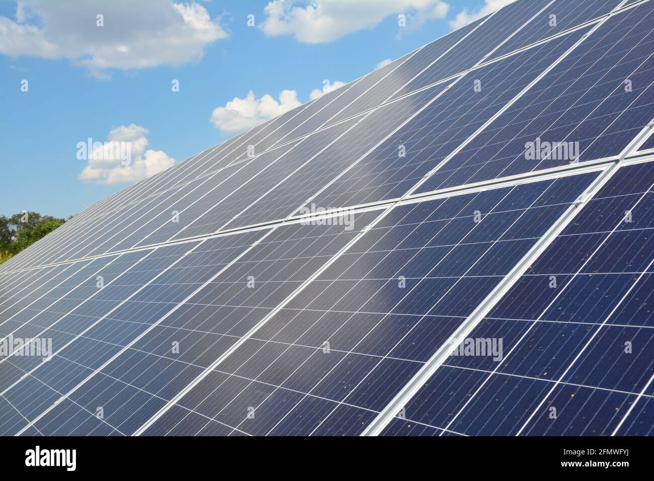 Un primo piano su un pannello solare con numerosi moduli solari e celle fotovoltaiche contro il cielo blu con nuvole bianche come fonte di energia alternativa. Foto Stock