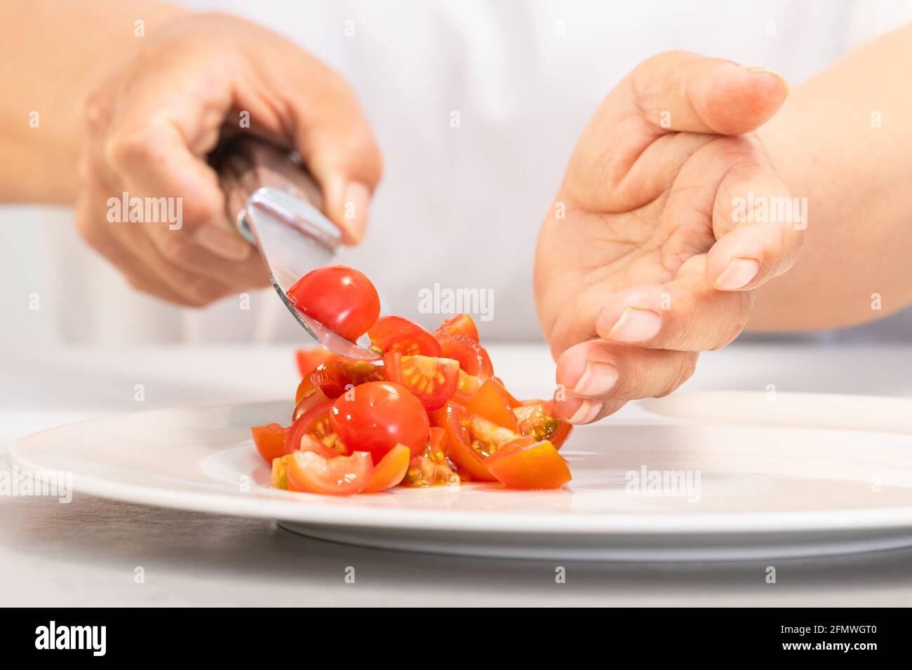Mani che cadono i pomodori appena tagliati su un piatto Foto Stock