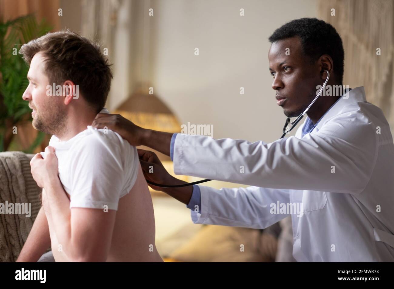 Medico africano che esamina i polmoni e il cuore dei giovani pazienti maschi che ascoltano Foto Stock