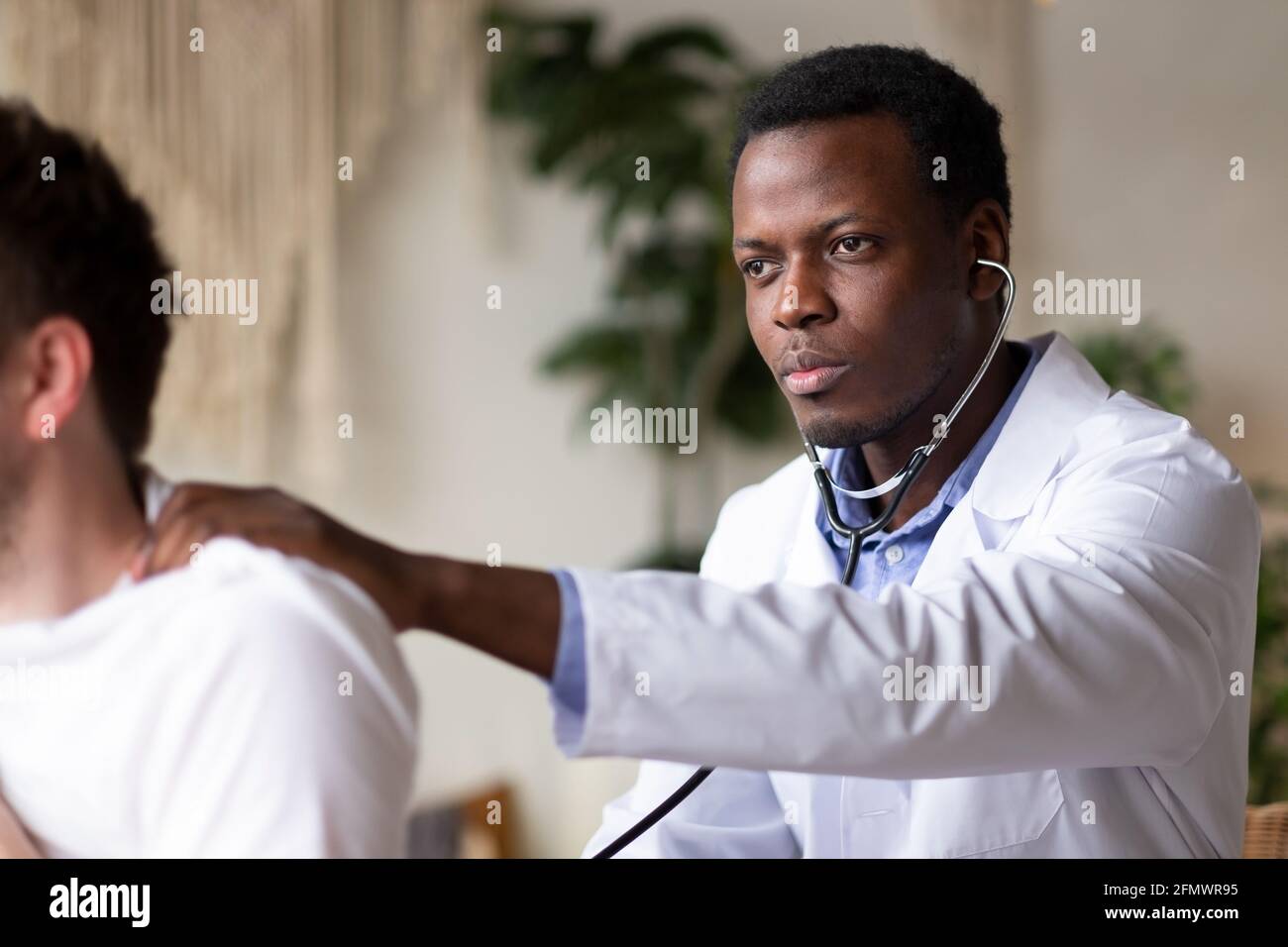 Medico africano che esamina i polmoni e il cuore dei giovani pazienti maschi che ascoltano Foto Stock
