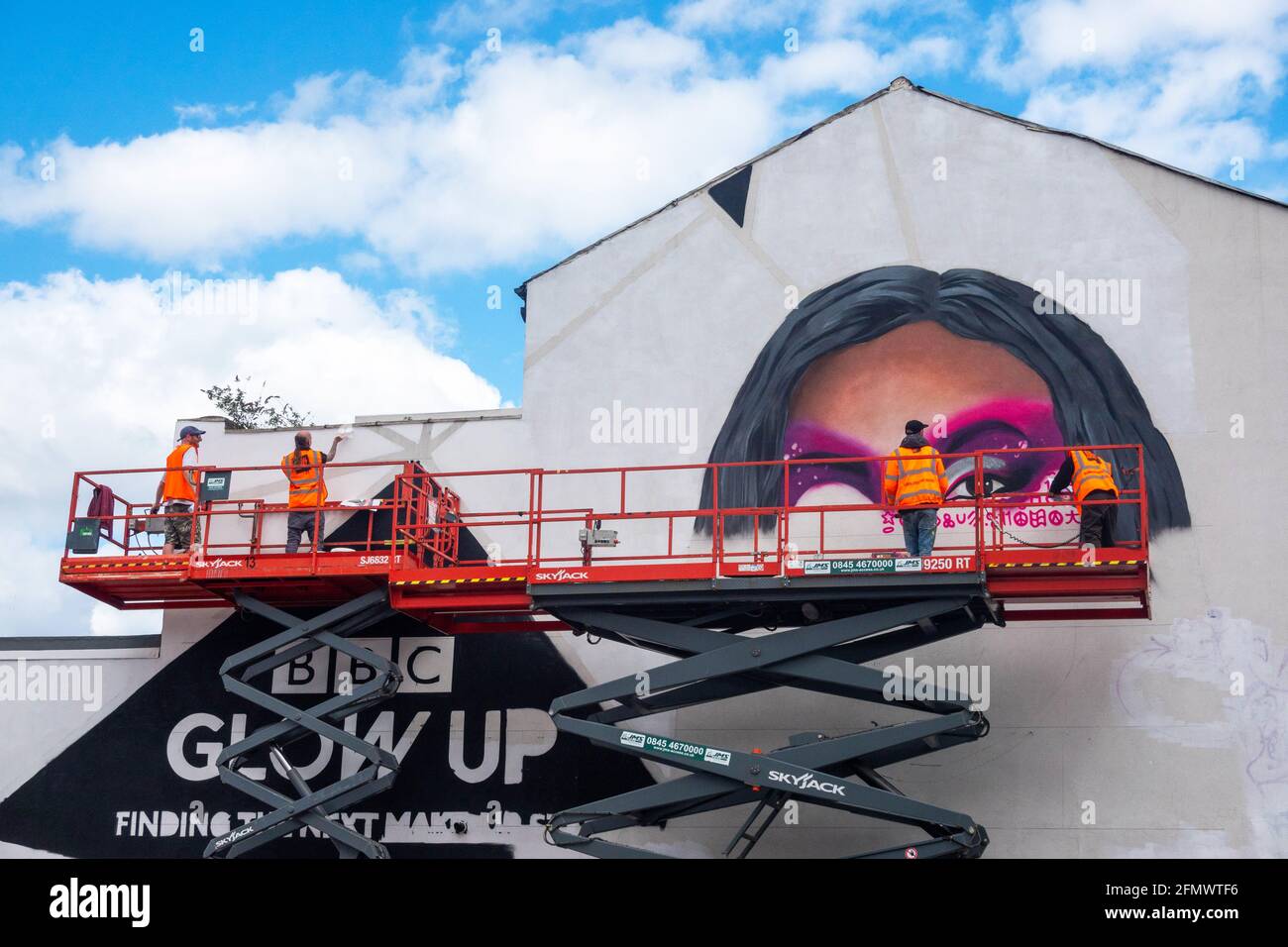 Un team di artisti murali di strada dipingendo un annuncio per la serie TV della BBC, Glow Up su un edificio a Liverpool Foto Stock