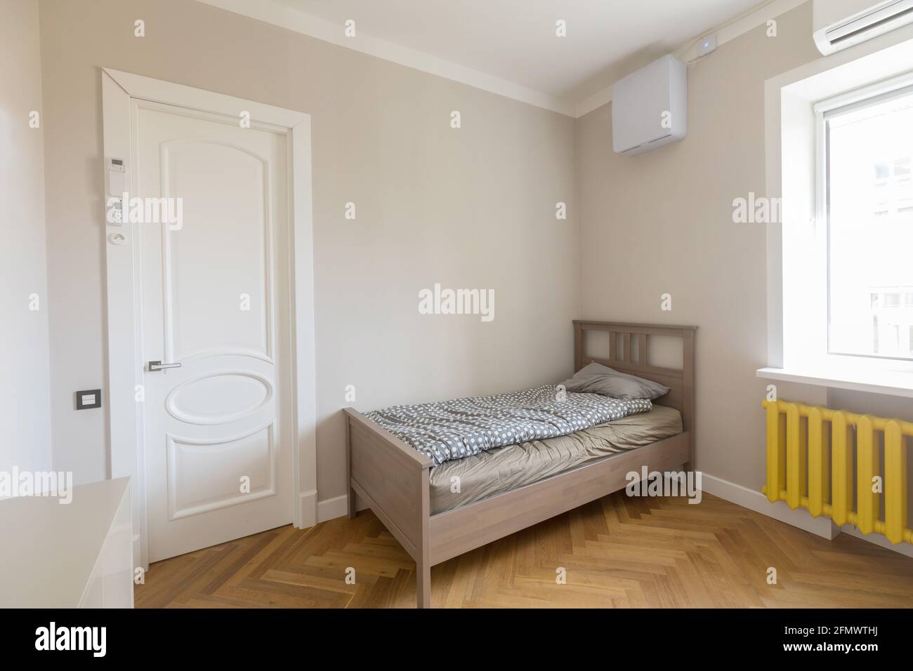Interni dallo stile minimalista di una camera da letto moderna e luminosa con legno letto singolo posto in angolo tra porta e finestra con radiatore giallo Foto Stock
