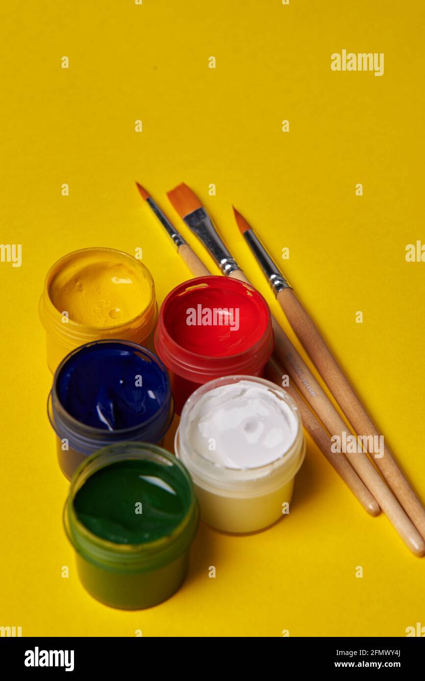 pennelli e lattine colorate di vernice su sfondo giallo Foto Stock