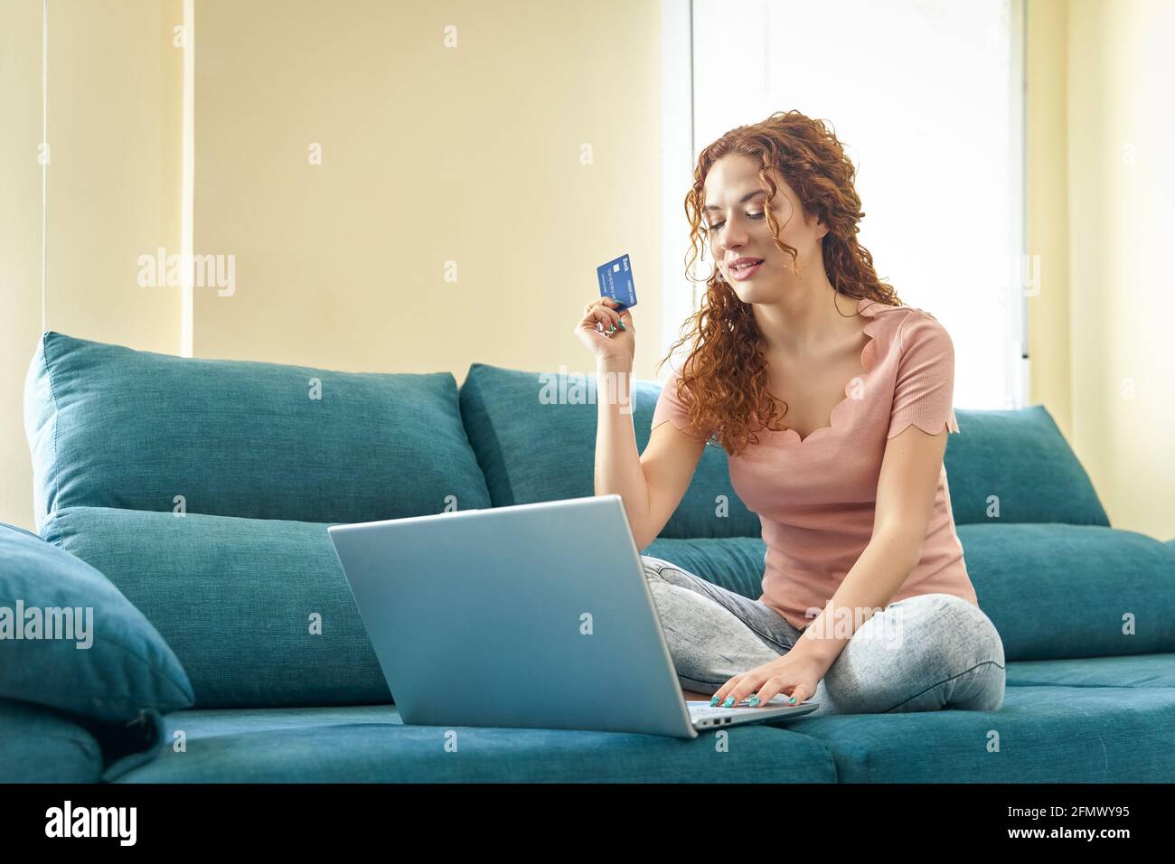 Sorridente ragazza millennial siede sul divano usando l'acquisto del laptop su Internet inserire i dettagli della carta di credito, concetto di servizio di sistema bancario facile. Foto di alta qualità Foto Stock