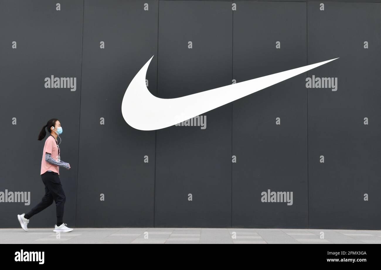 Una donna che indossa una maschera del viso passa accanto al logo Nike e al  negozio in Wangfujing Street a Pechino Foto stock - Alamy