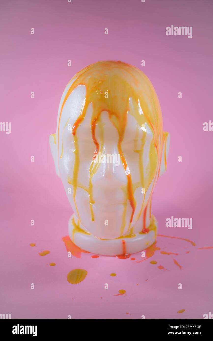 Busto del viso umano coperto di vernice gialla e rossa. Su sfondo rosa tenue. Minimal concetto astratto di moda, make up e stile. Foto Stock