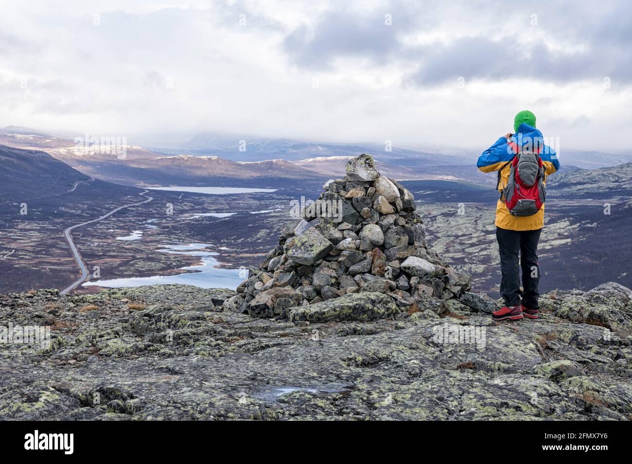 Dopo una pioggia nel tardo autunno un uomo si trova accanto ad un mucchio di pietre sulla cima di Mehøe e guarda nella valle con i suoi laghi. Parco Nazionale di Dovre Foto Stock