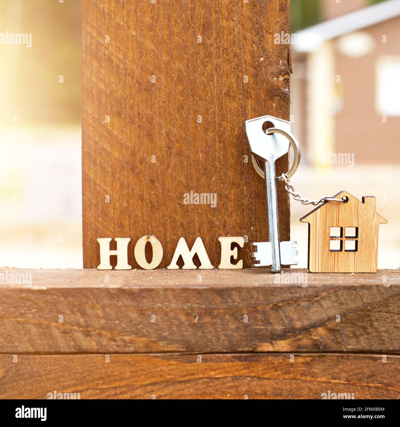 Portachiavi di casa in legno su recinzione con chiave e iscrizione in lettere inglesi 'home'. Cottage sullo sfondo. Costruzione, progetto, spostamento a n Foto Stock