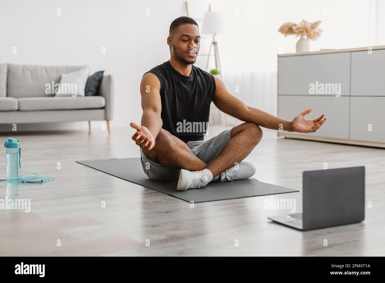 Il guy afroamericano che fa lo yoga al laptop che medita a casa Foto Stock