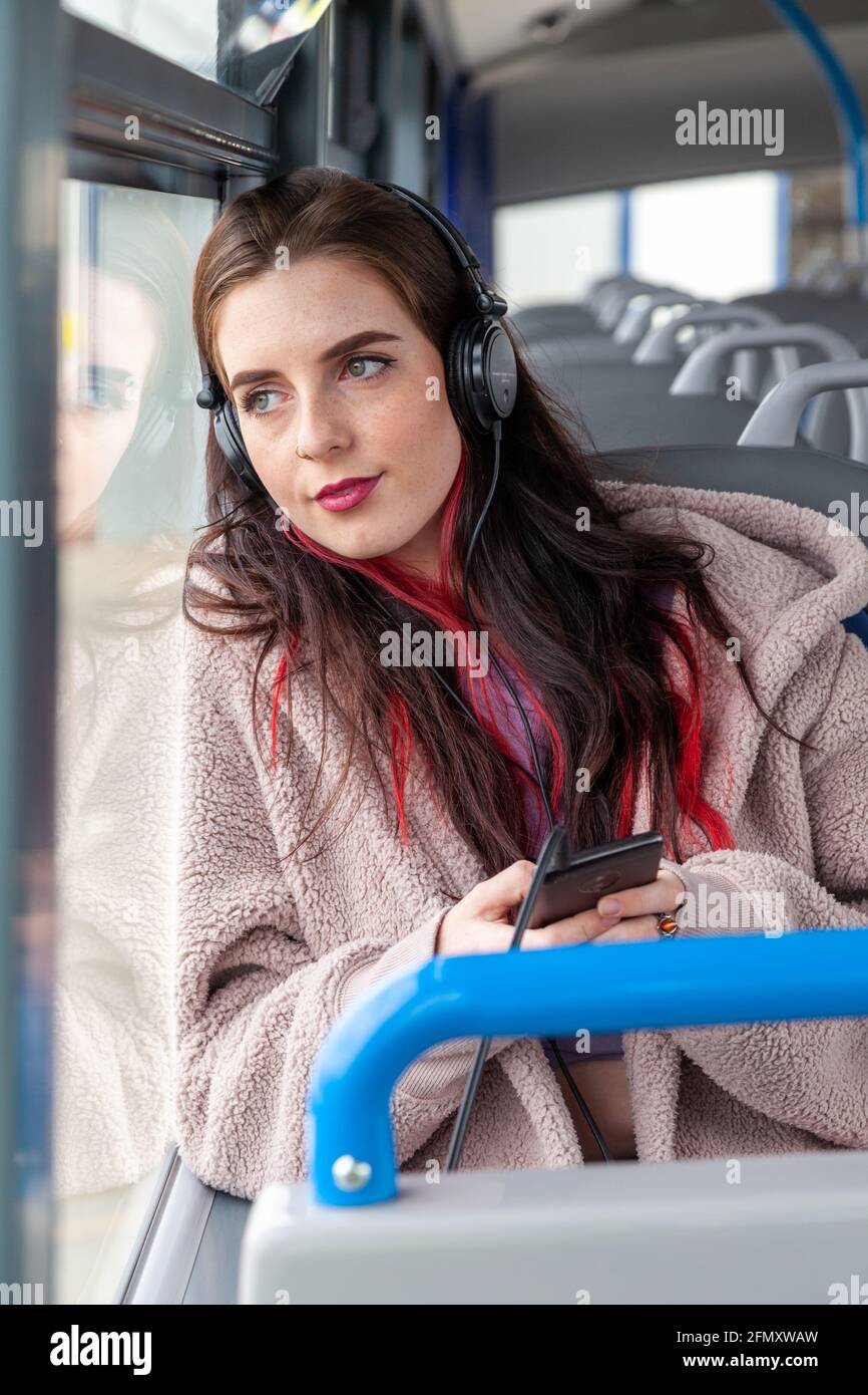 Una bella giovane donna seduta su un autobus ascoltare musica attraverso gli auricolari e guardando fuori dalla finestra Foto Stock