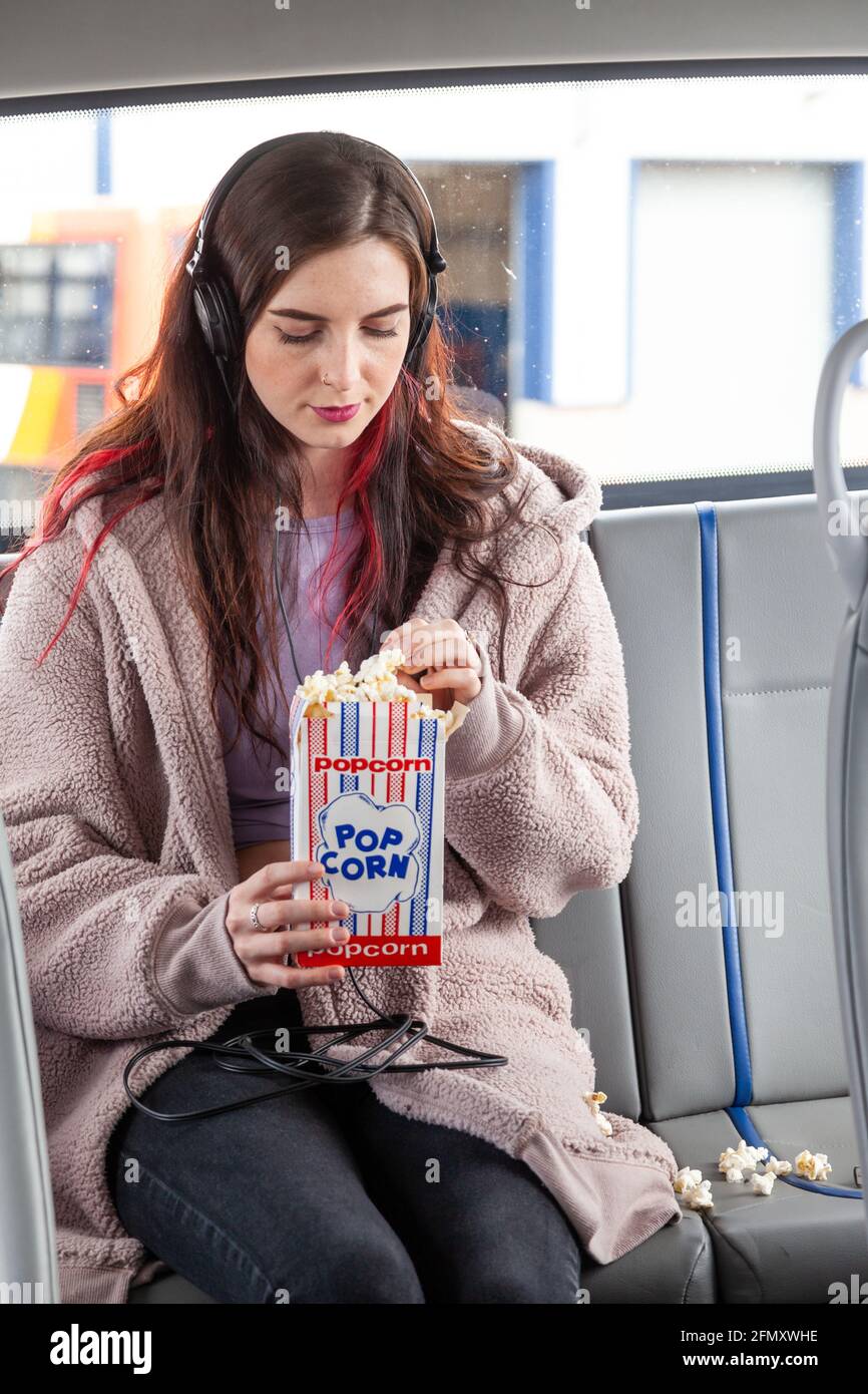 Una giovane donna che mangia popcorn sul sedile posteriore di un autobus Foto Stock