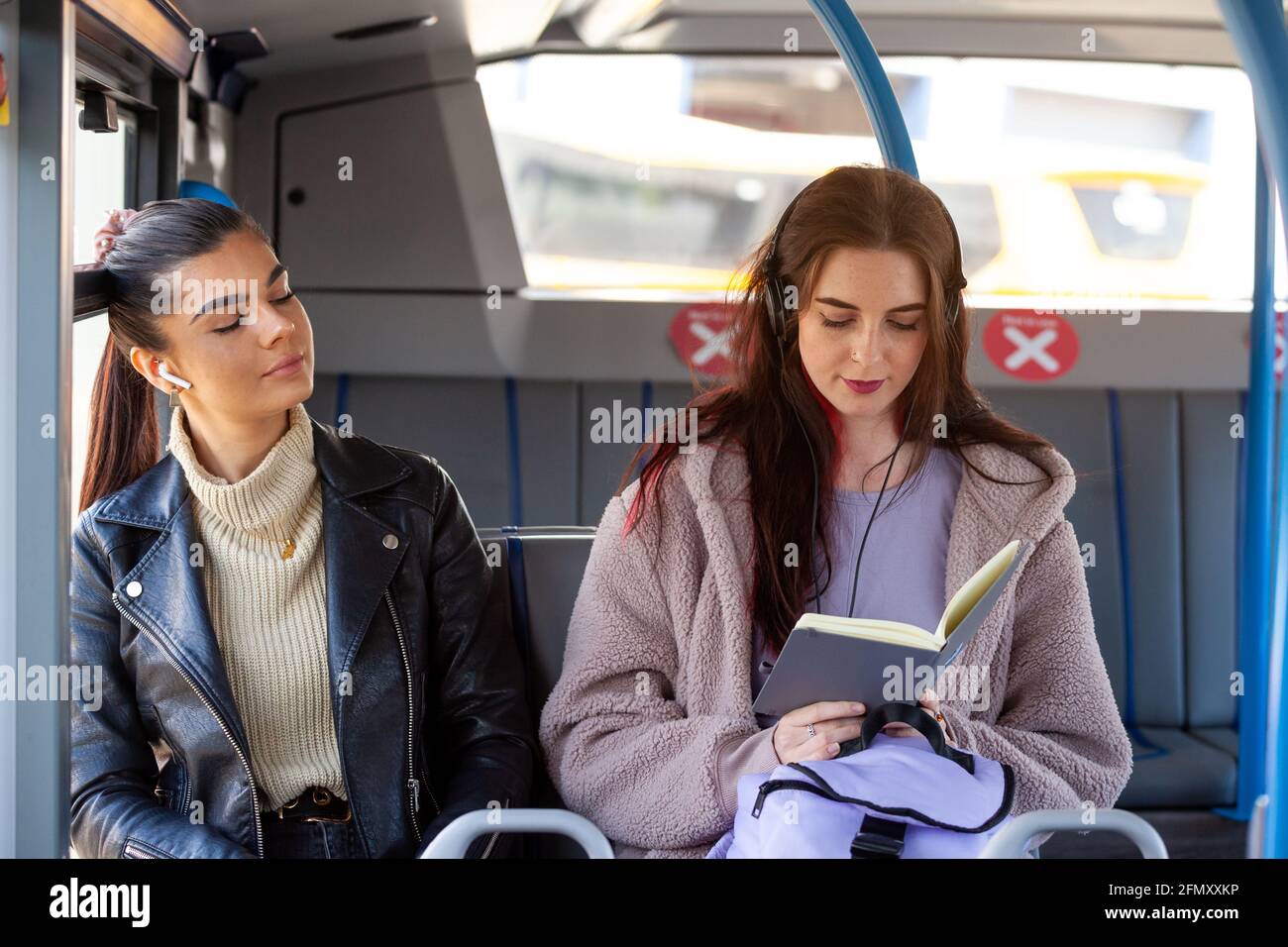 due donne che viaggiano su un autobus che ascoltano musica e uno che legge anche un libro Foto Stock
