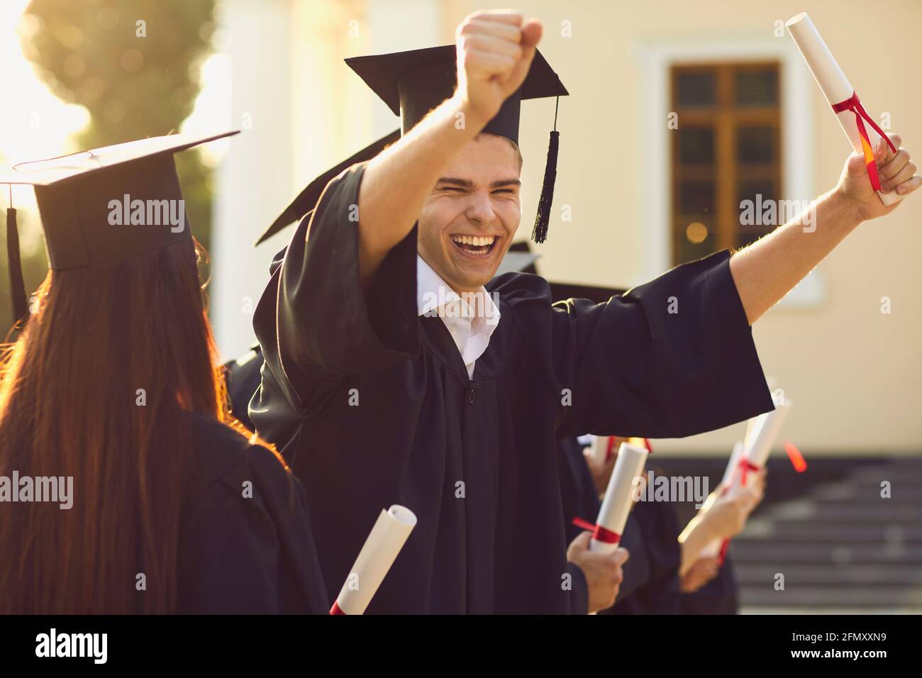 Felice sorridente laureato in mantle che tiene il diploma in alzato mano ed esprimere felicità Foto Stock