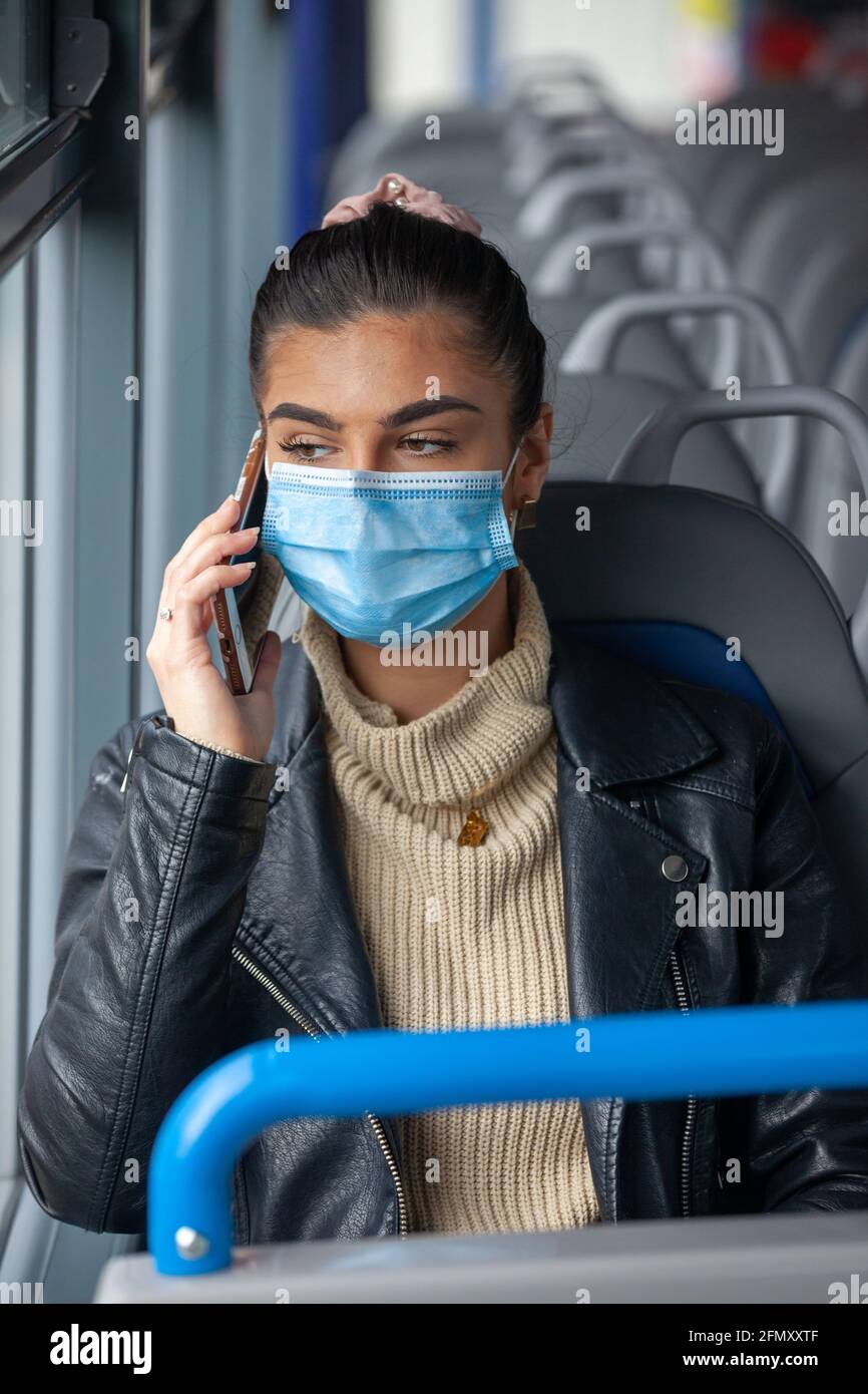 Donna che viaggia su un autobus indossando una maschera facciale e che parla su un telefono cellulare. Foto Stock
