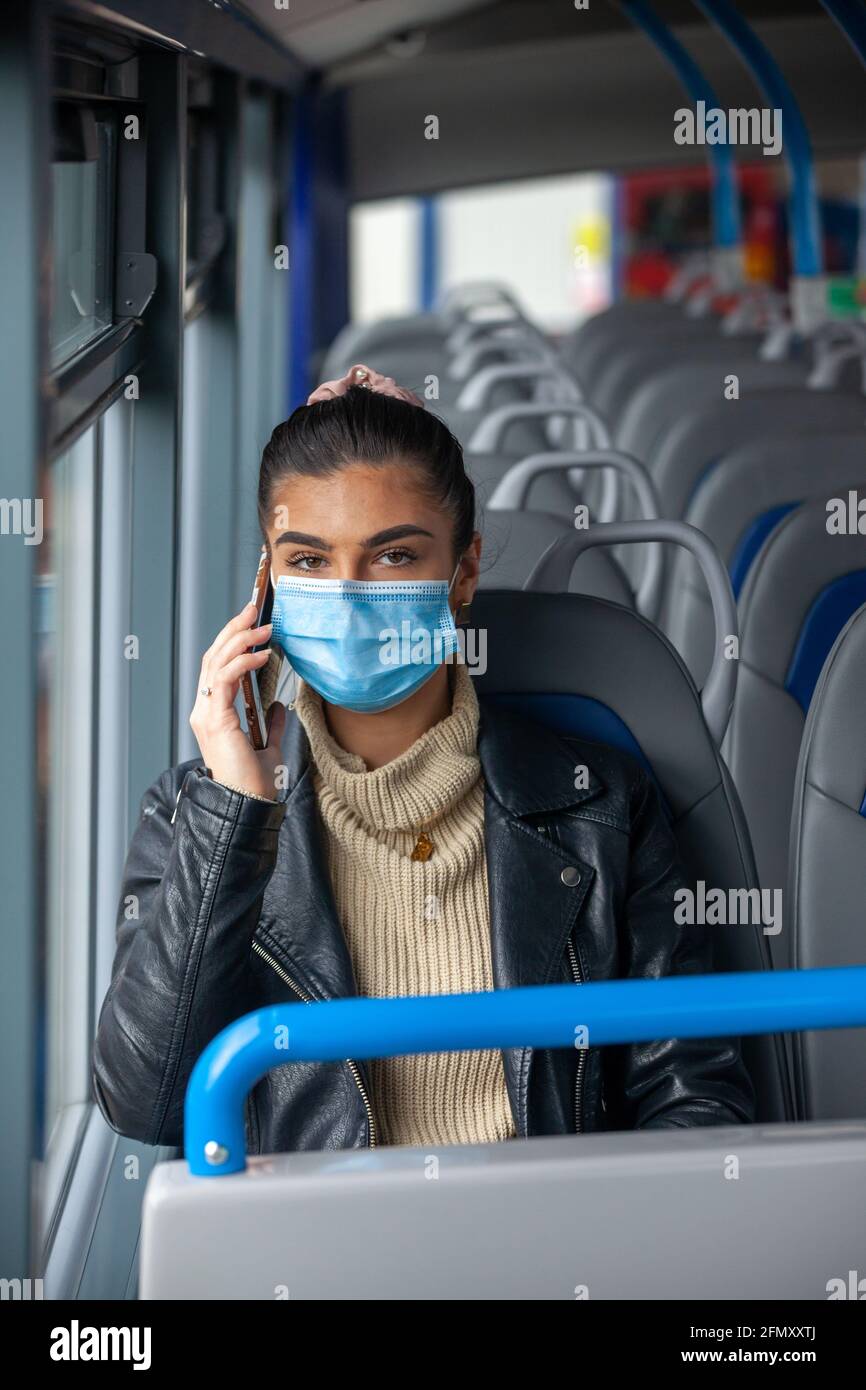 Donna che viaggia su un autobus indossando una maschera facciale e che parla su un telefono cellulare. Foto Stock