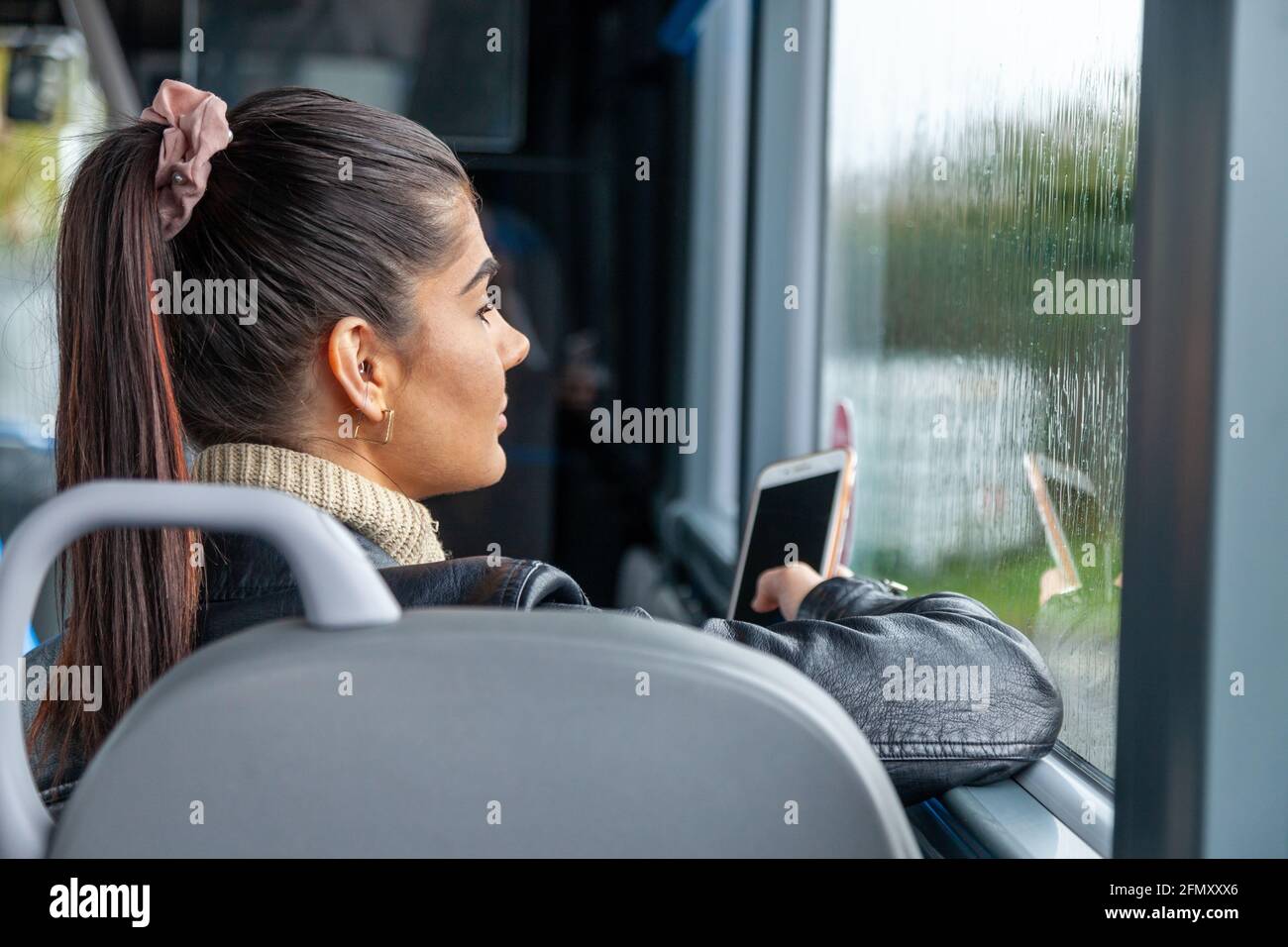Una donna che viaggia in autobus e guarda fuori dalla finestra bagnata dalla pioggia. Foto Stock