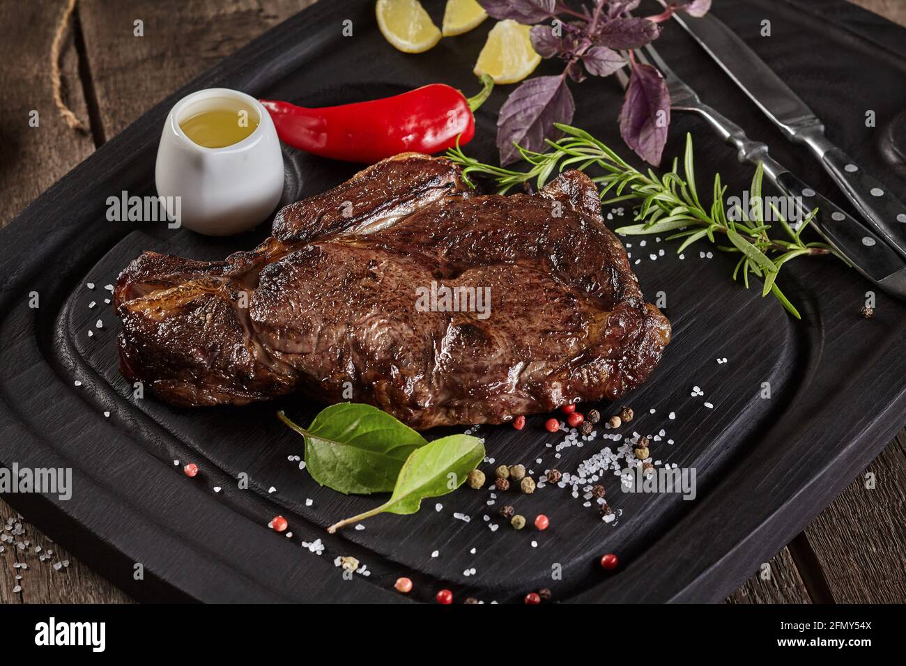 Closeup di bistecca di vitello arrosto con condimenti su tavola di servizio con posate Foto Stock