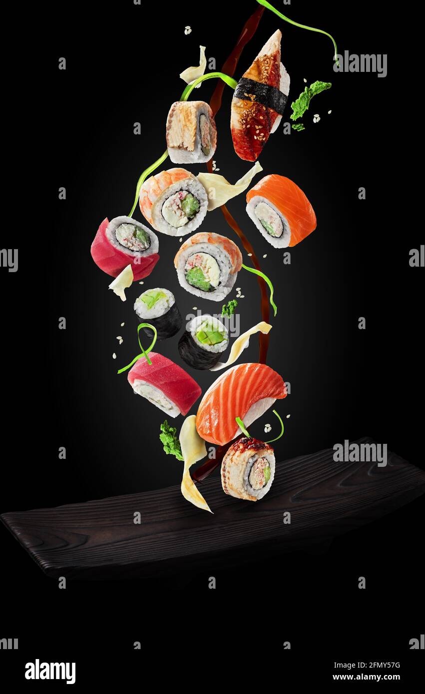 Sushi con guarnire e salsa di soia che si snodano sul piatto sfondo nero Foto Stock