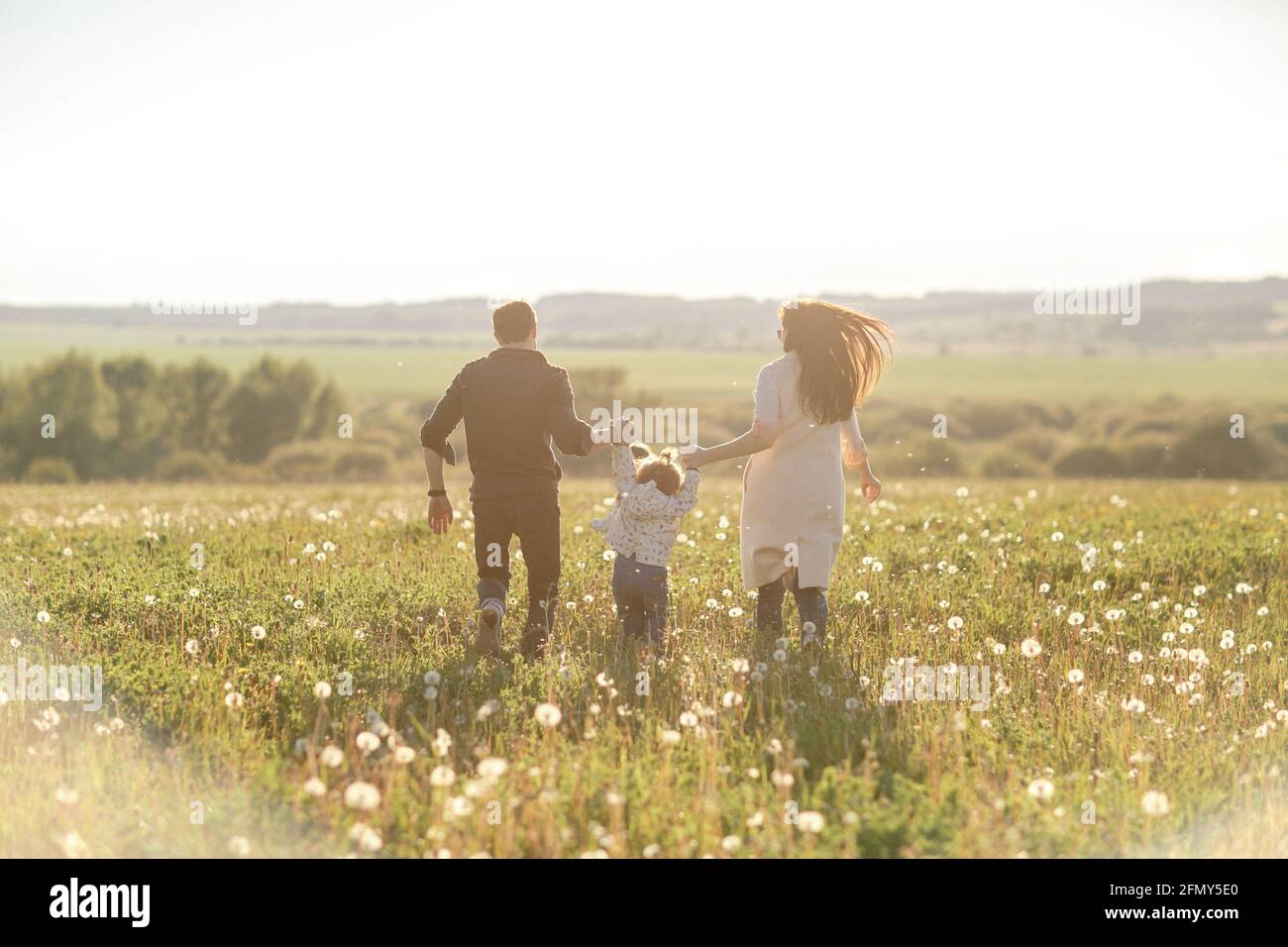 Famiglia felice che corre attraverso il campo. Papà, mamma e due figlie Foto Stock
