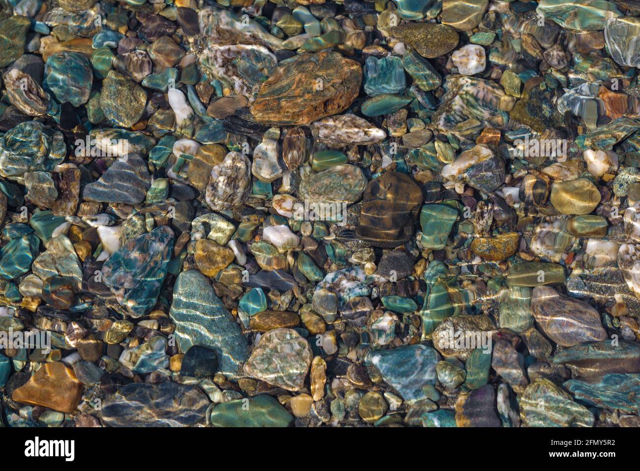 Ciottoli colorati in fondo a un fiume poco profondo una giornata di sole Foto Stock