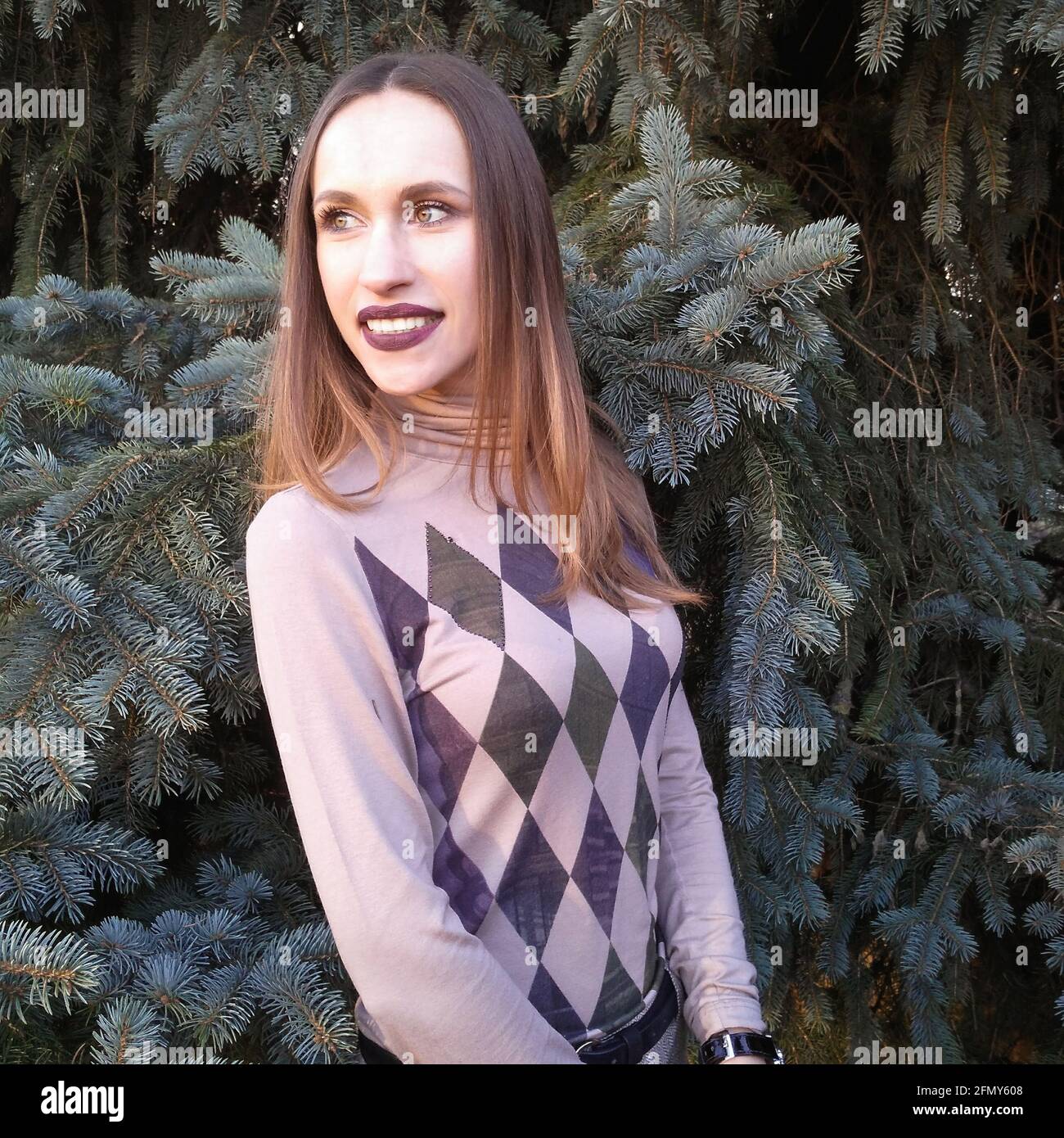 Attraente giovane donna tra aghi abete sorride e guarda a sinistra Foto Stock