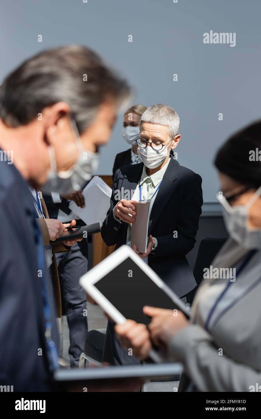 fuoco selettivo di donna d'affari matura con i documenti vicino ai colleghi con tablet digitale in primo piano sfocato Foto Stock