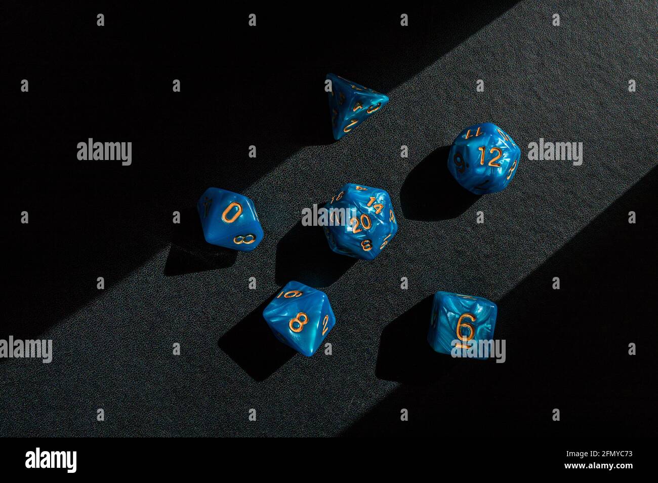 Set di dadi di gioco di ruolo blu marmorizzati su un nero superficie illuminata da un fascio di luce solare Foto Stock