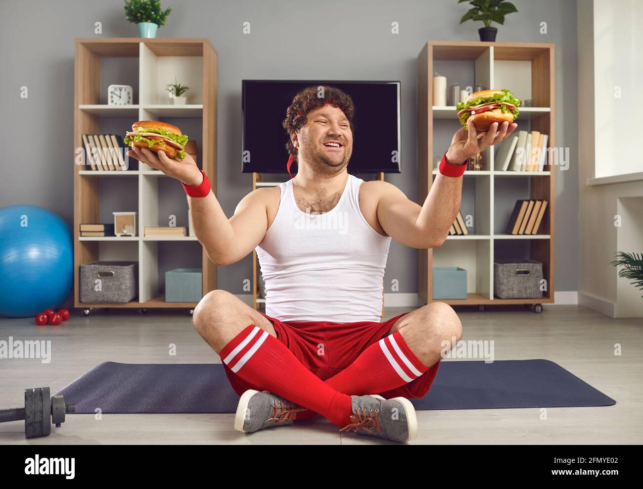Uomo millenario eccitato con corpo chubby che tiene hamburger fast food in due mani Foto Stock