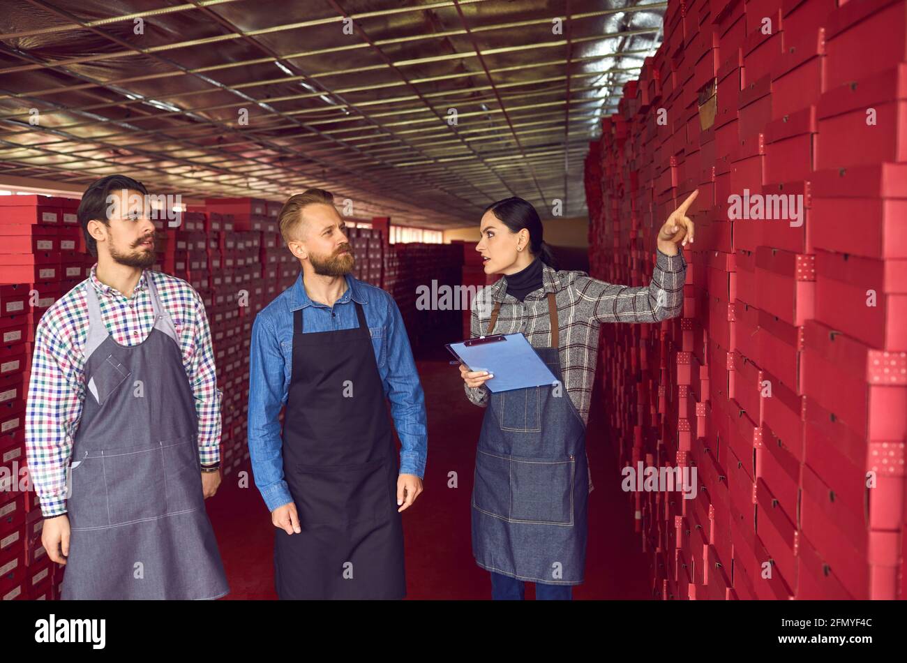 Responsabile del magazzino della fabbrica di calzature che parla con i lavoratori in piedi quasi a lungo file di scatole per calzature Foto Stock