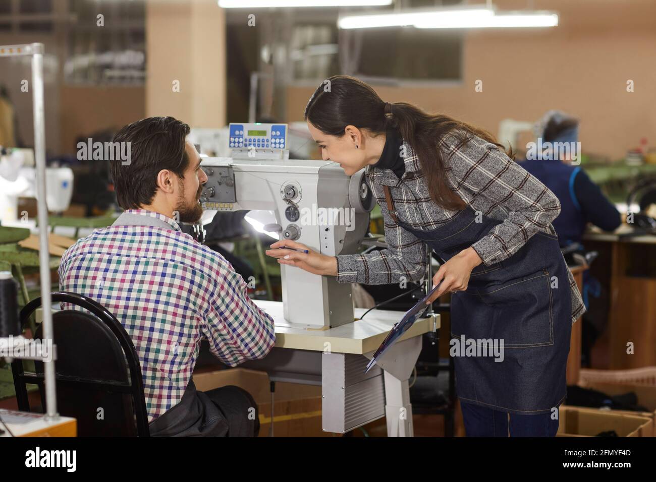 Due operai della fabbrica di scarpe che parlano ad un tavolo con un macchina per cucire scarpe industriali Foto Stock