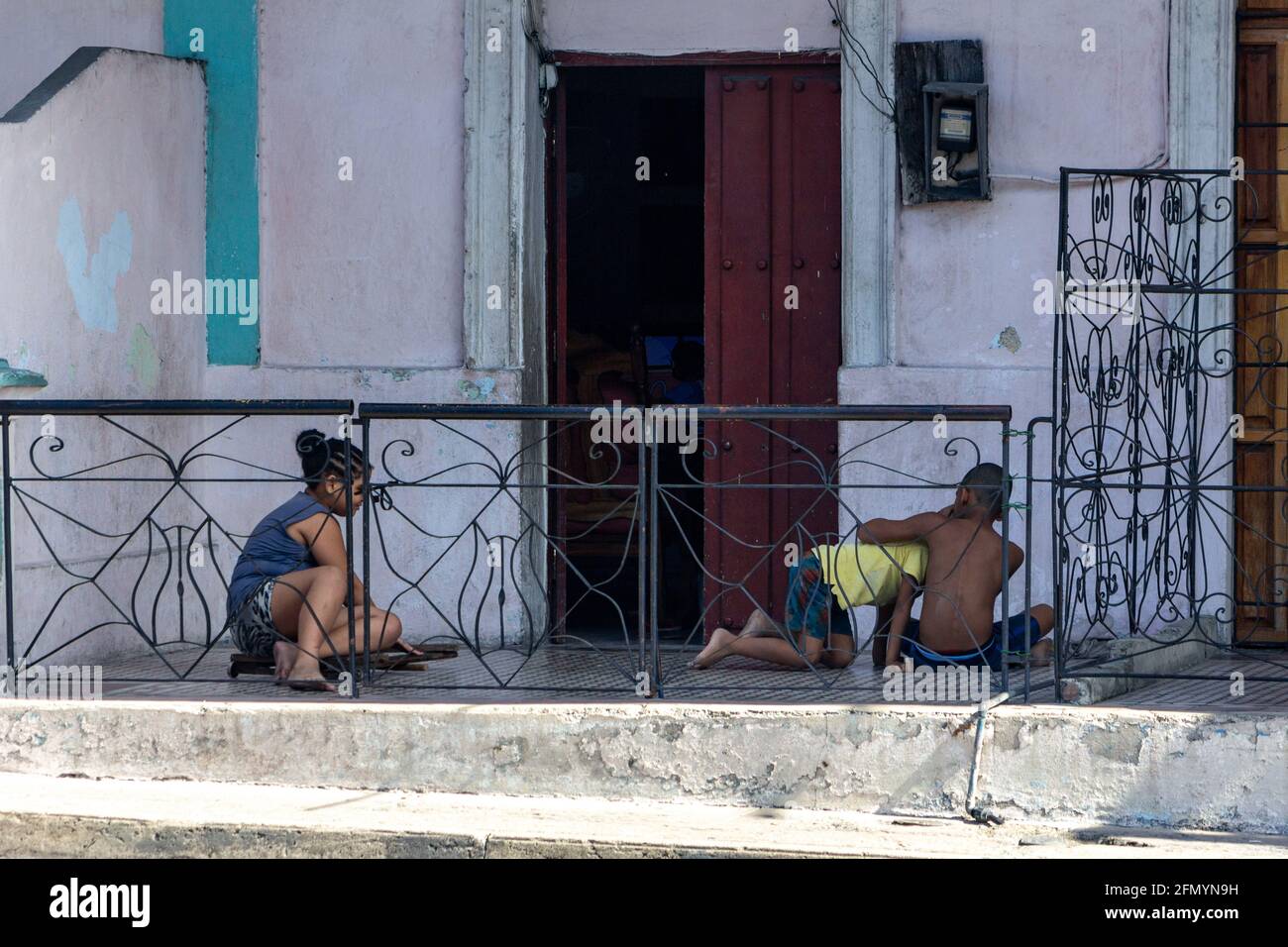 Bambini cubani che giocano in un portico di una vecchia casa intemperie. Stile di vita a Santiago de Cuba, Cuba Foto Stock
