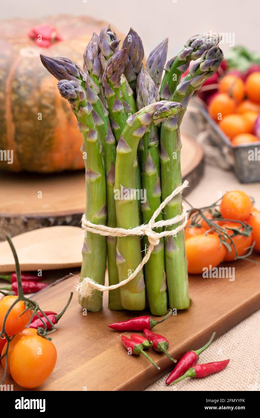 Asparagi verdi freschi isolati su vecchio tavolo di legno con pomodori e. una zucca Foto Stock