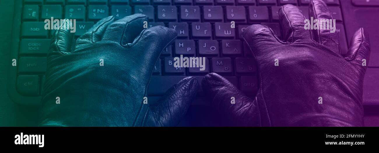 Cybercriminale, guanti a mani in mano sulla tastiera del computer portatile, foto con tonalità al neon. Foto Stock