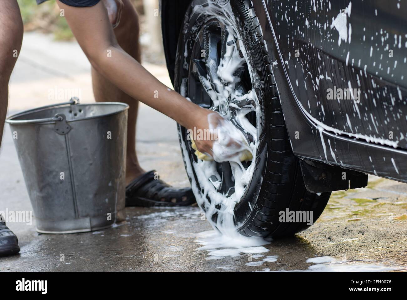 Ruota lavamani dell'auto con acqua saponata. Uomo pulisce l'auto con spugna, acqua e detergente. Foto Stock