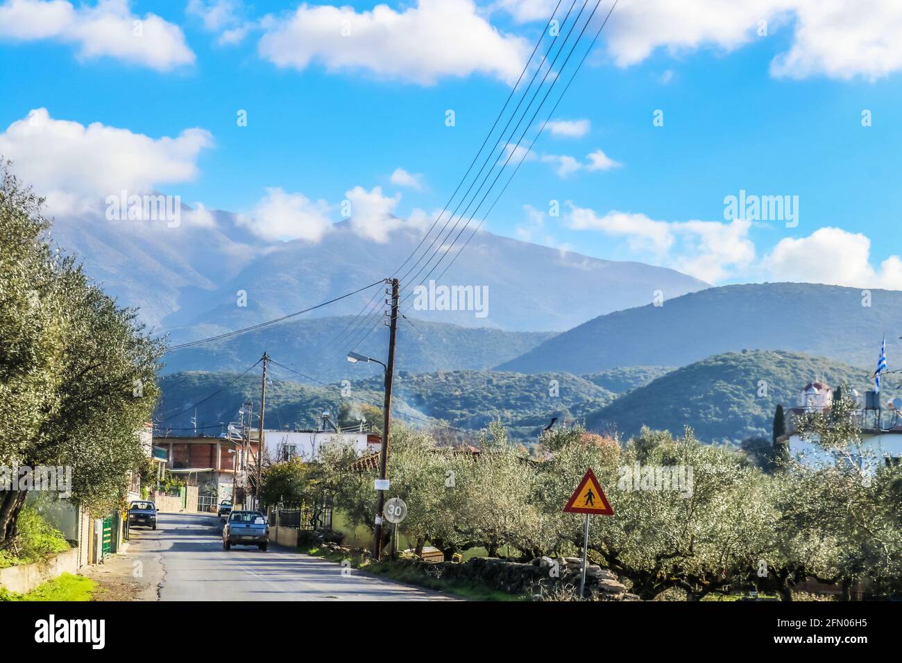 Guida attraverso un piccolo villaggio di montagna nella catena montuosa di Taygetus in La penisola del Peloponneso, nel sud della Grecia, con alberi di olivo e. abete potato Foto Stock