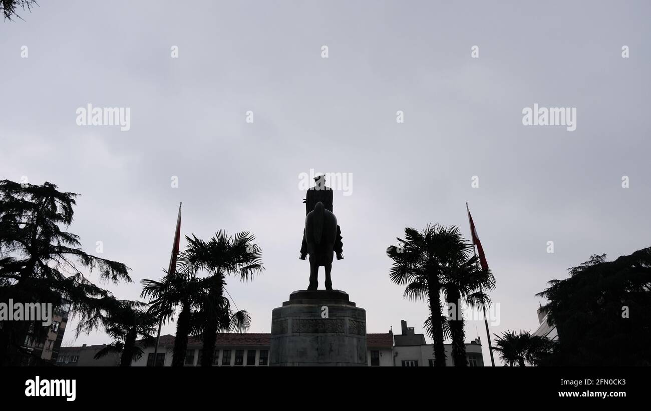 Scultura di Ataturk fondatore della Repubblica Turca nel centro di Bursa (heykel) durante il tempo piovoso e sovrastato con bandiera turca e scultura coperta Foto Stock