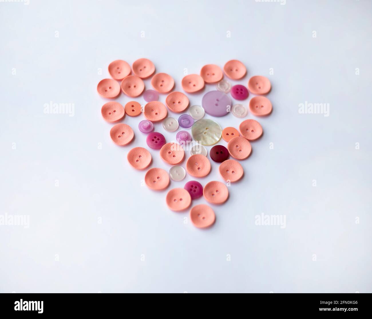 Bottoni di diverse dimensioni in tonalità di rosa sono disposti a forma di cuore. Sfondo bianco. Progettazione. Foto Stock