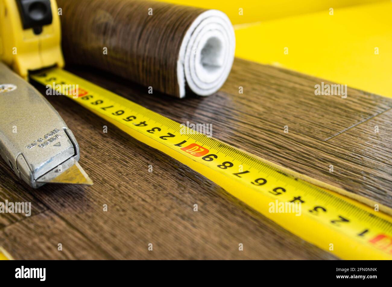 Metro a nastro in linoleum e coltello su fondo isolato. Un pezzo di linoleum. Misurazione e taglio del linoleum. Linoleum per pavimenti in PVC. Galleggiamento domestico Foto Stock