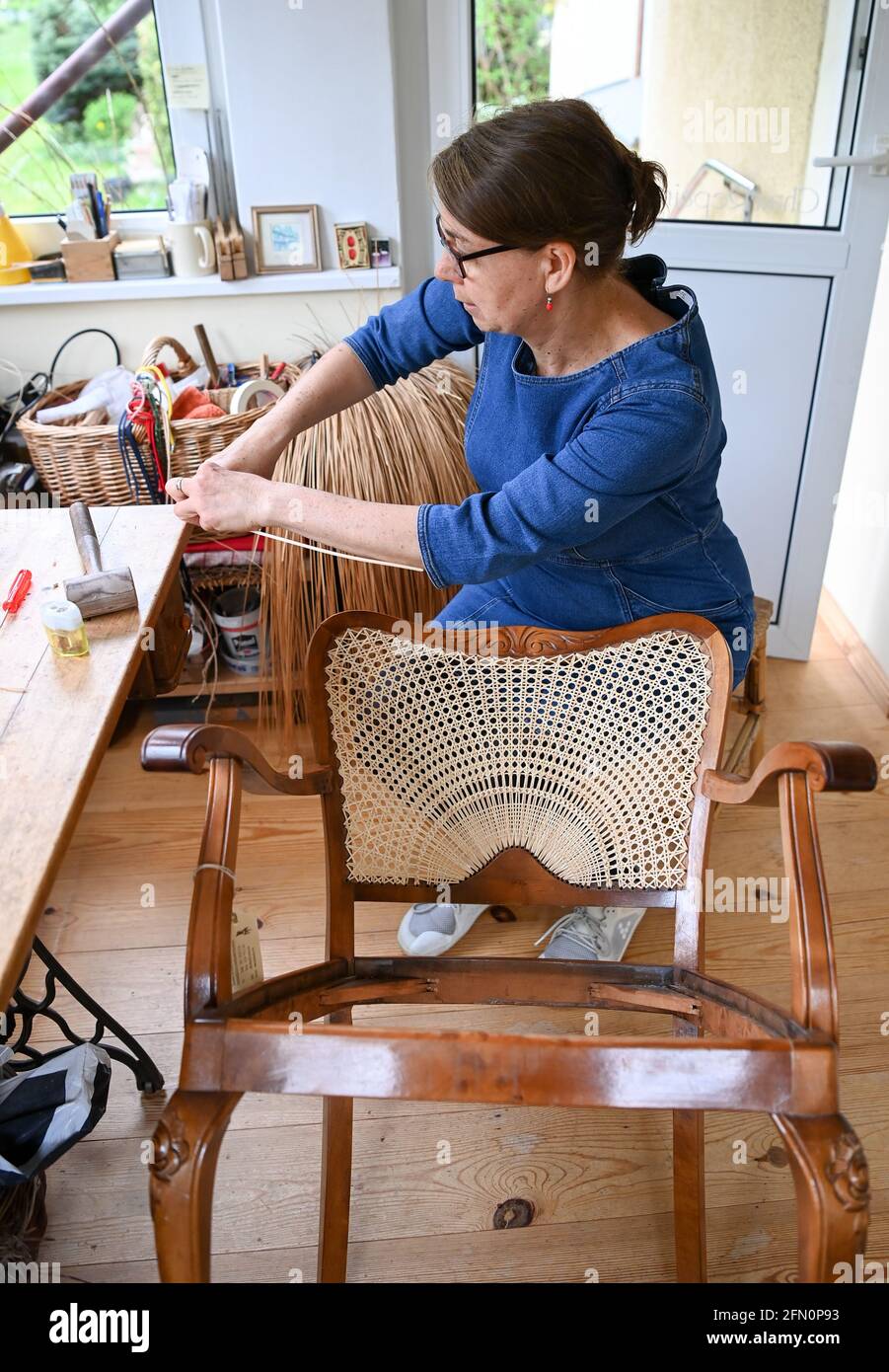 Berlino, Germania. 12 maggio 2021. Tessitore di sedia Silke Schlittermann  lavora alla riparazione di una poltrona con armatura a metà sole nella sua  officina a Köpenick. La sedia che tondola la canna,