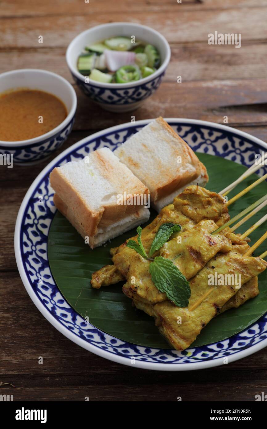 Satay di maiale cibo tailandese locale con salsa di salsa di oeanut immersione isolato su sfondo di legno Foto Stock