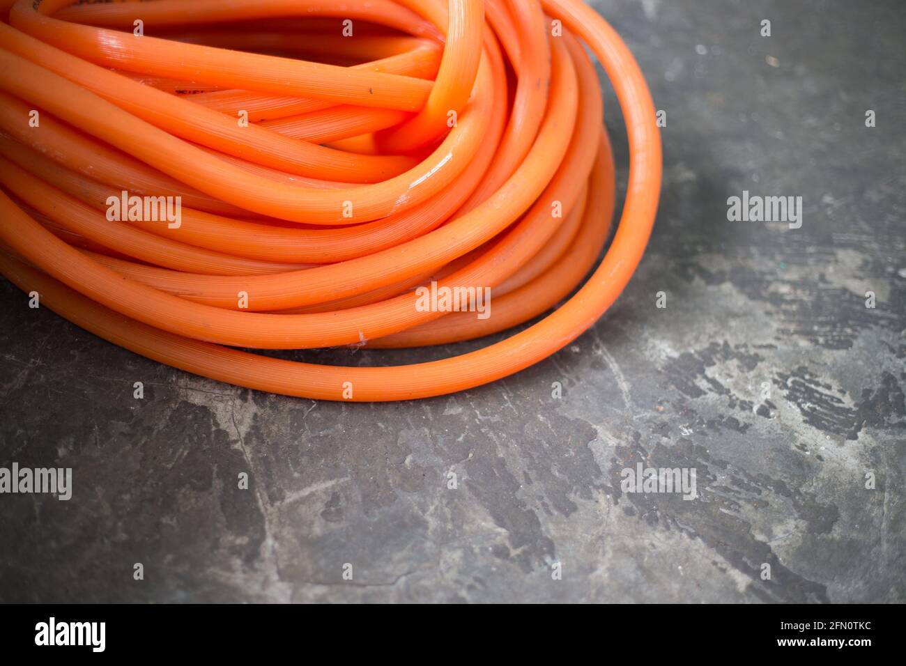 Colpo di closeup del tubo di gomma arancione arrotolato sulla superficie di calcestruzzo Foto Stock